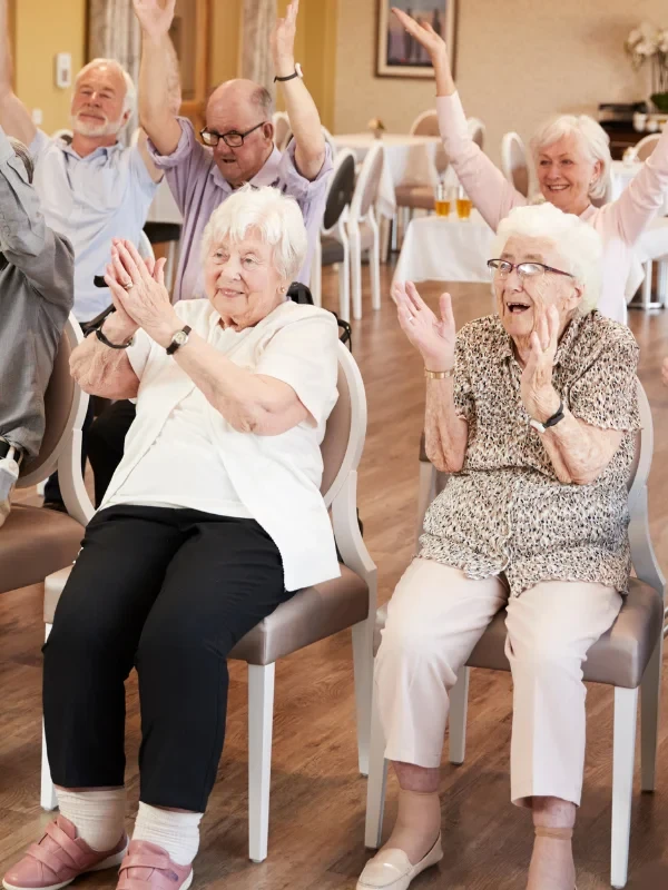 Elderly residents clapping and enjoying an engaging activity together at an assisted living facility.