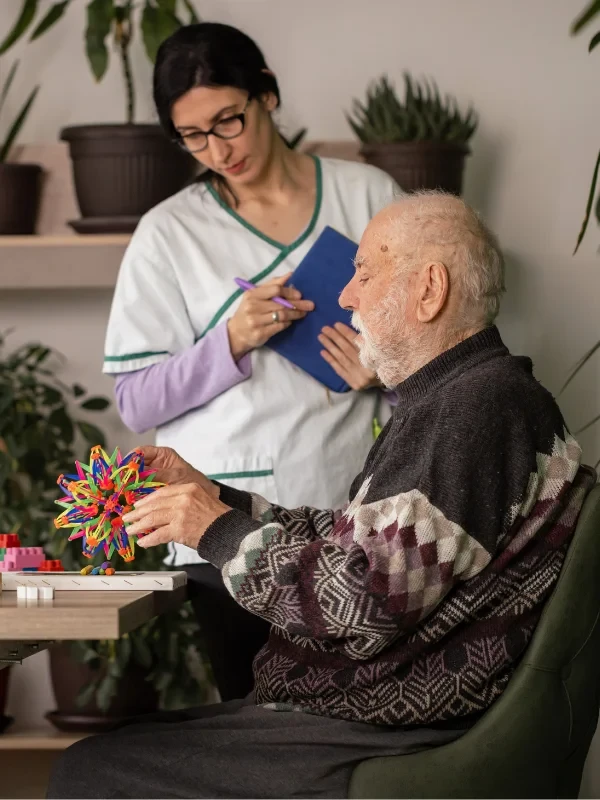 Caregiver assisting an elderly man with a colorful therapy toy, providing specialized care in a nurturing environment.