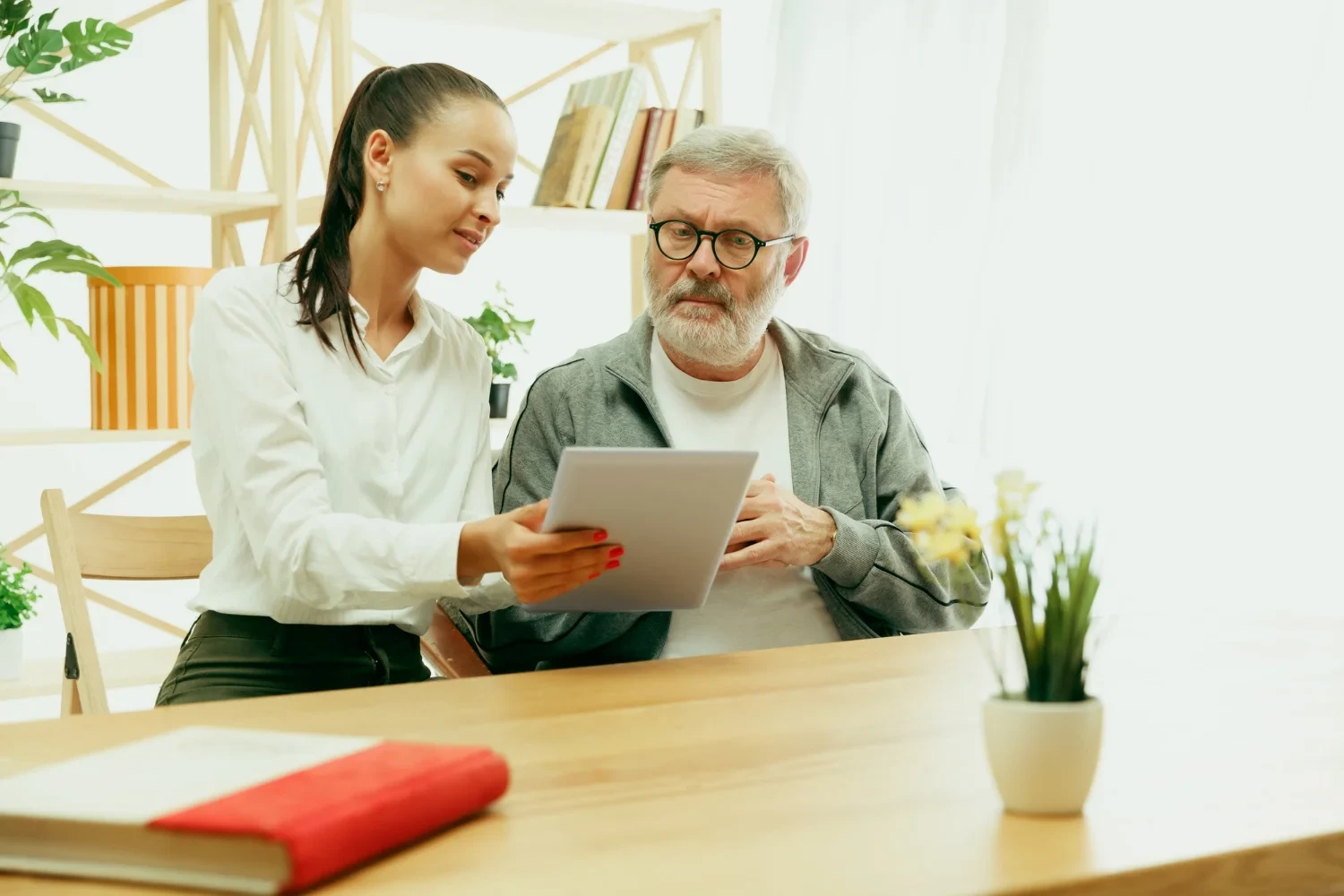 Caregiver assisting elderly man with a tablet, offering support and guidance in a comfortable living room.