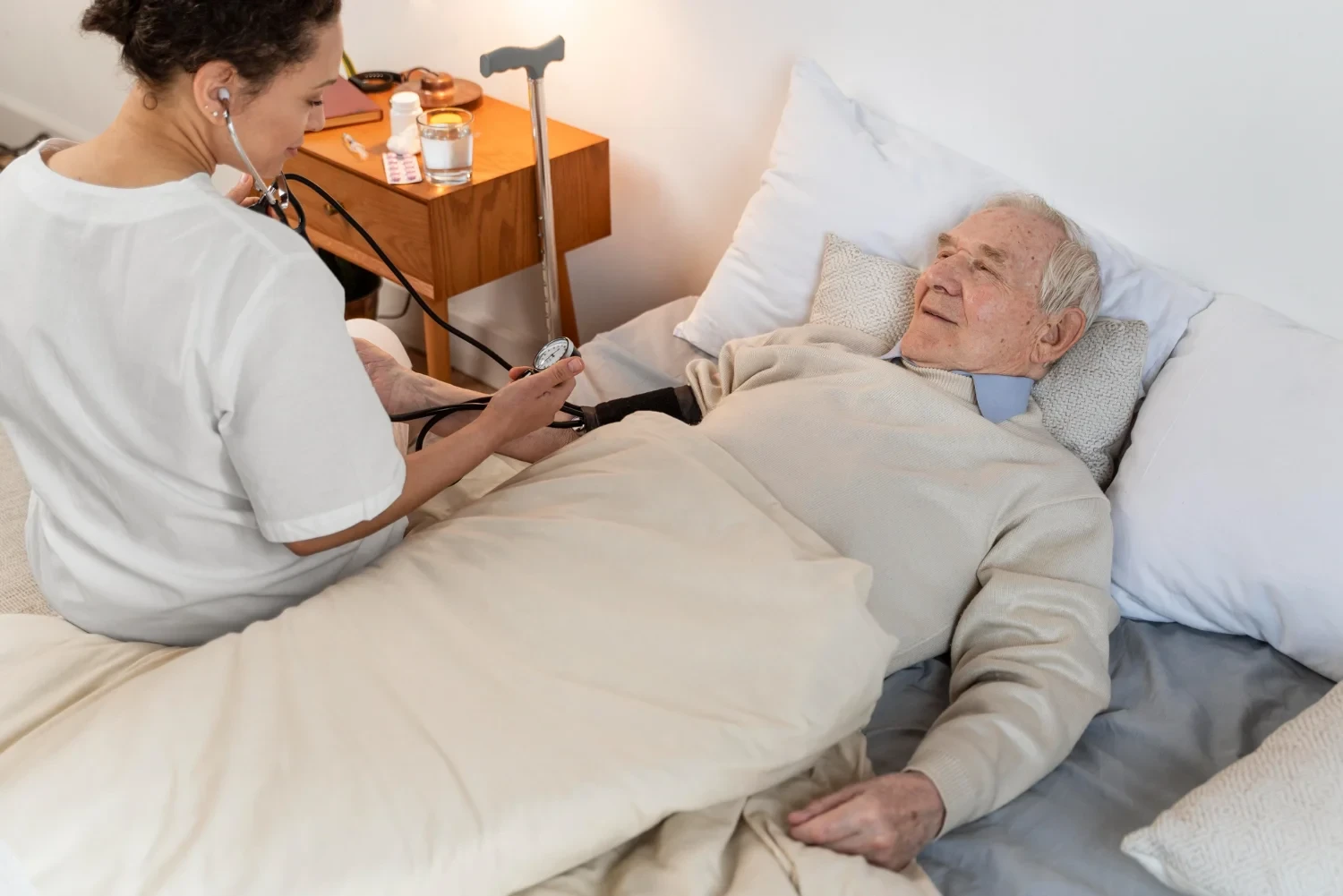 Caregiver checking vital signs of an elderly man in a cozy bedroom, providing personalized hospice care.