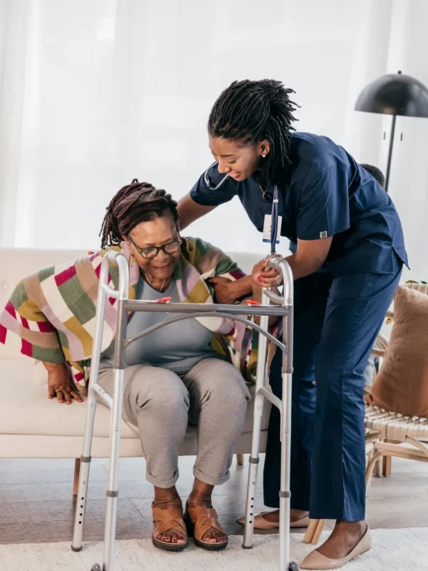 A caregiver helping an elderly woman using a walker, providing support and care in a safe environment.