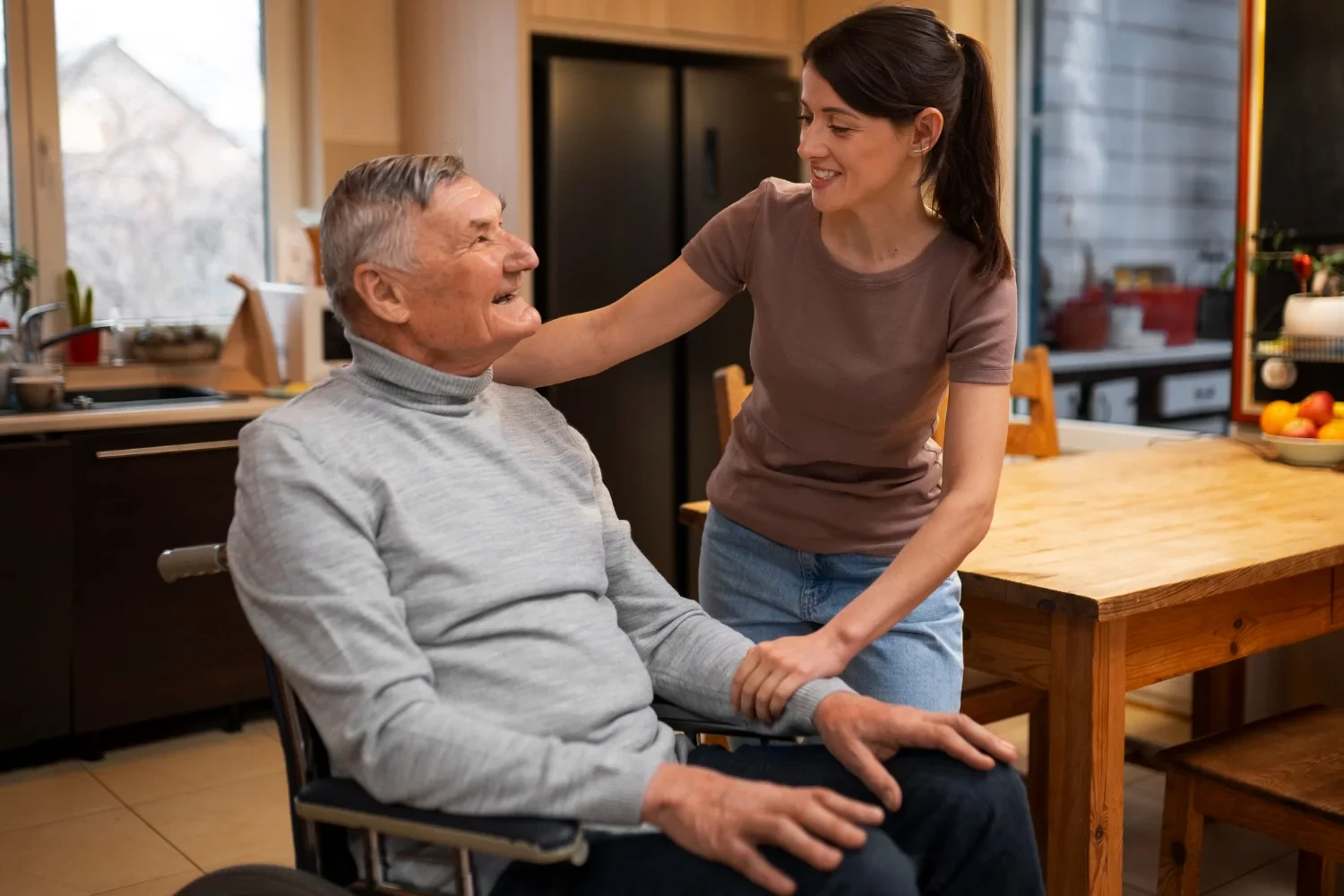 Caregiver smiling while talking to elderly man sitting comfortably at home kitchen table