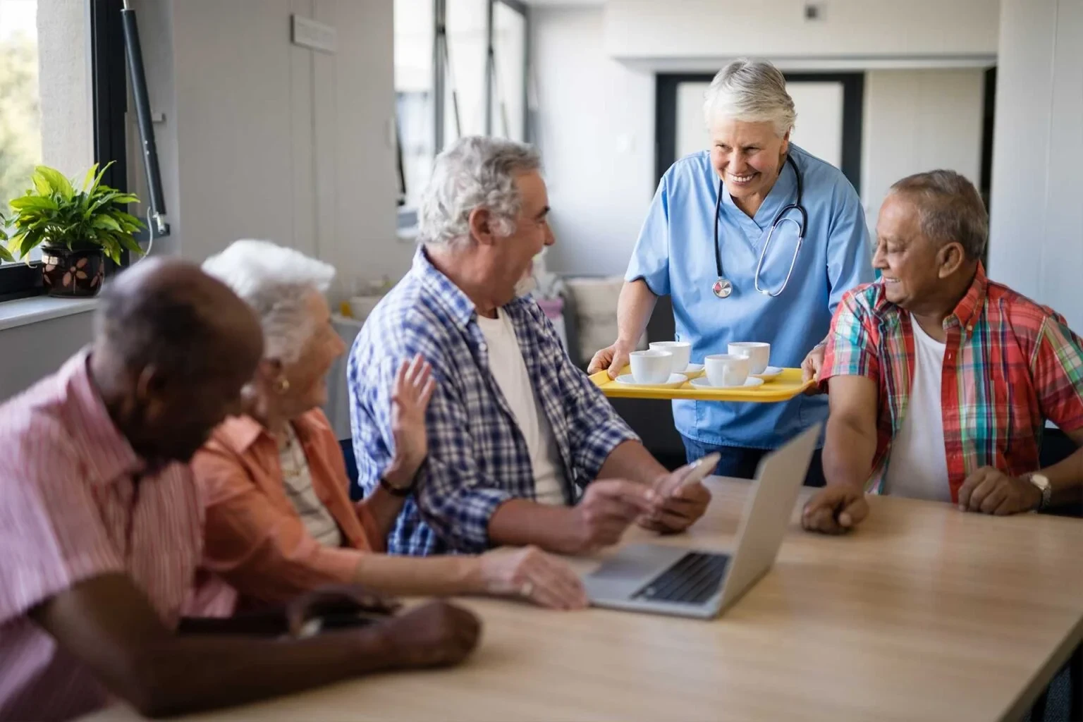 Group of elderly residents enjoying a meal in a communal dining area, with a caregiver in a welcoming atmosphere.