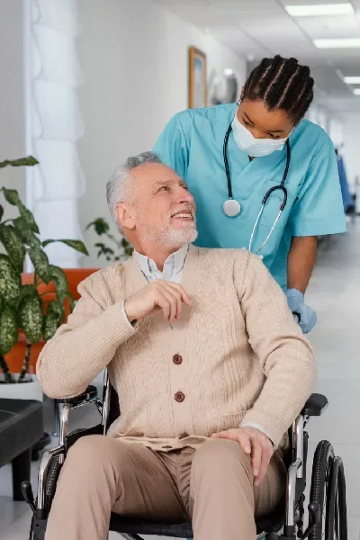 Nurse offering compassionate support to a smiling senior man in a wheelchair at Elite Care Assisted Living Facility in Lakeland, Florida.