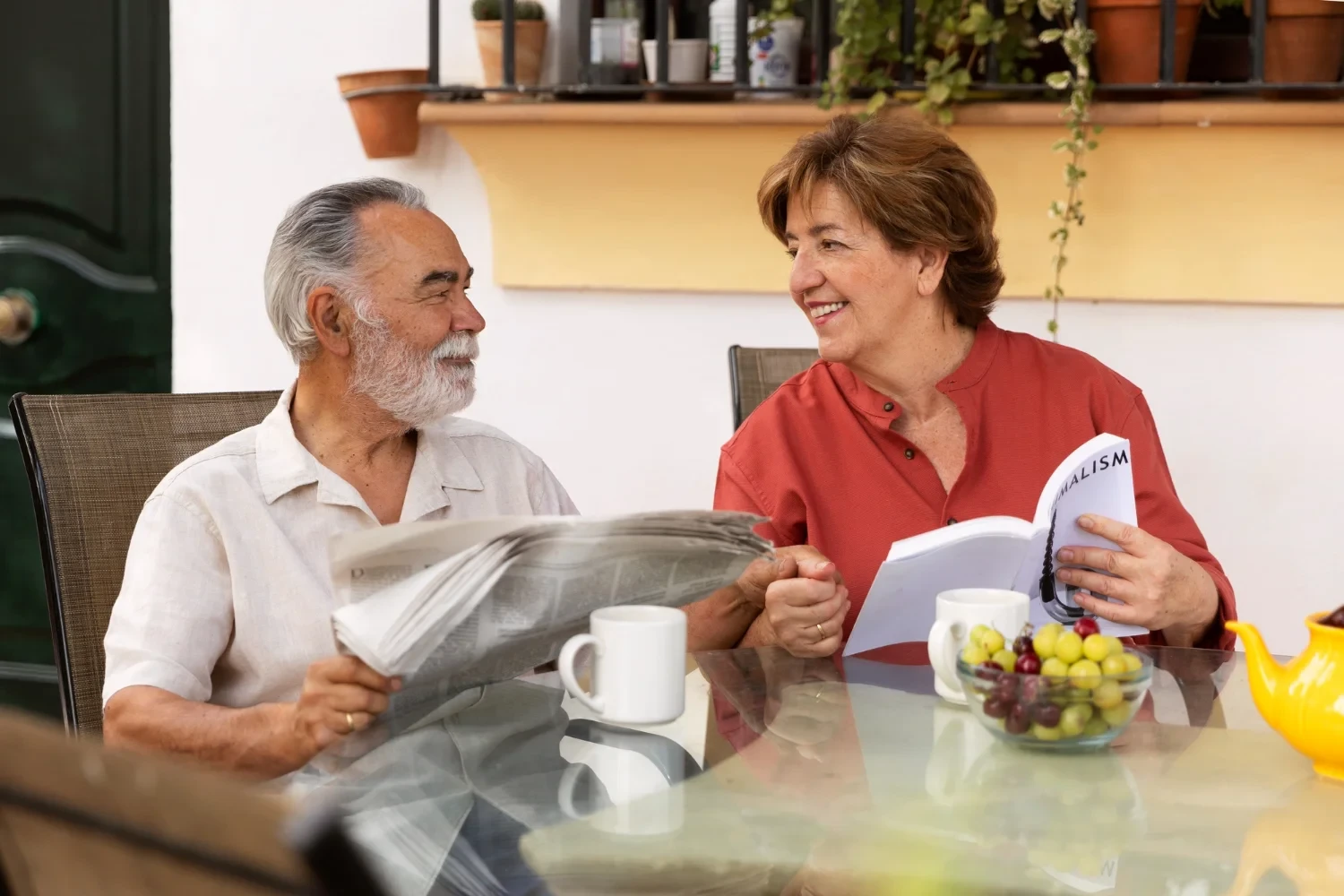 Elderly couple enjoying coffee and reading newspaper on outdoor patio with plants in background
