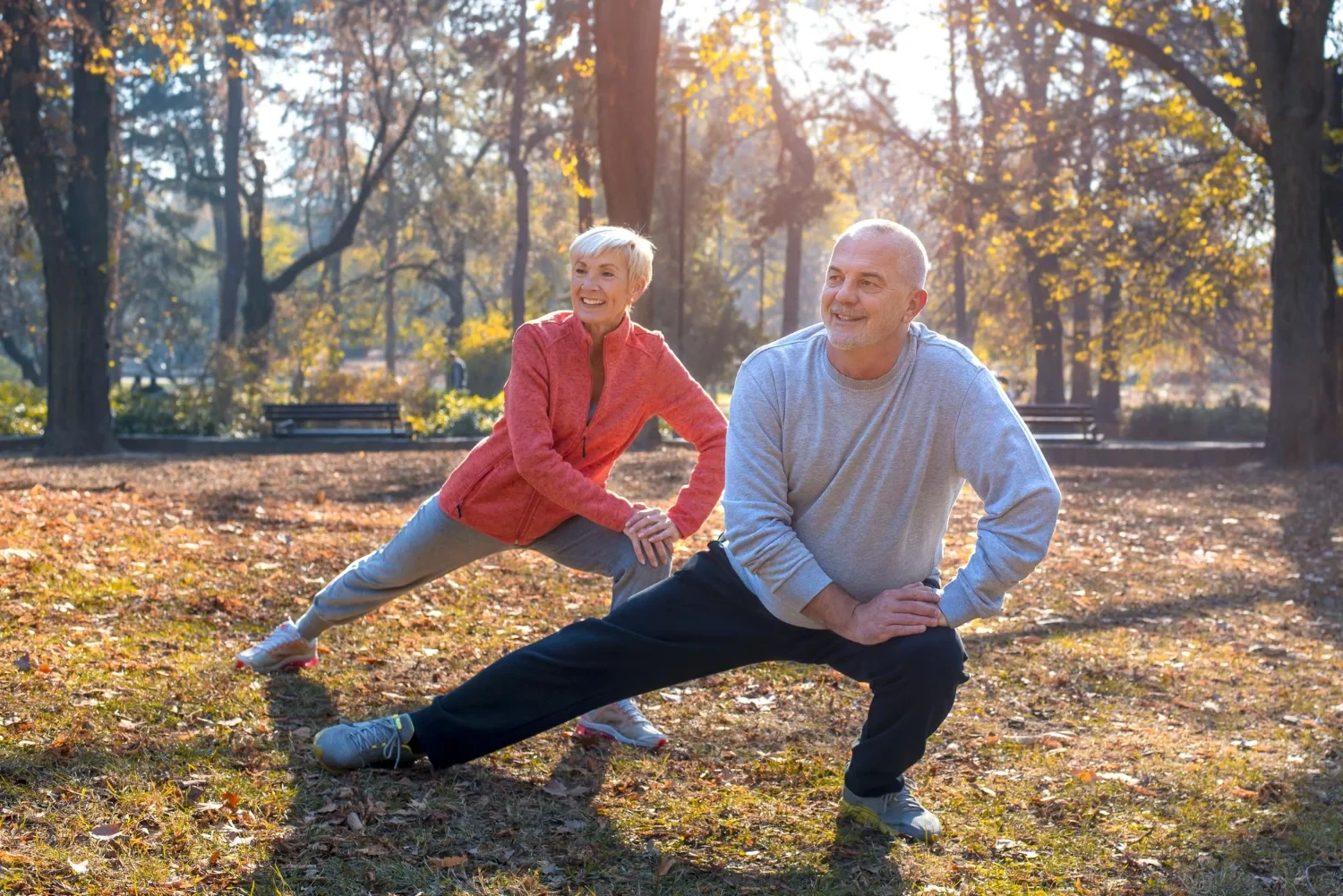 An elderly couple stretching outdoors during a fitness session, promoting physical wellness at an assisted living facility.
