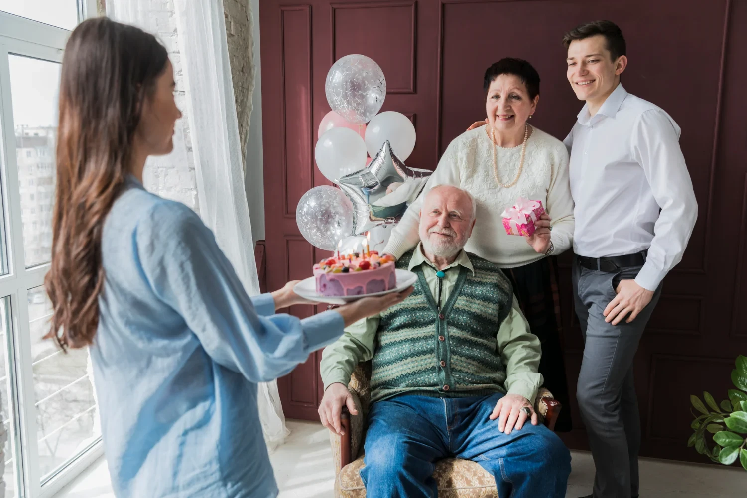 A family celebrating an elderly man’s birthday with cake and gifts in a cheerful indoor