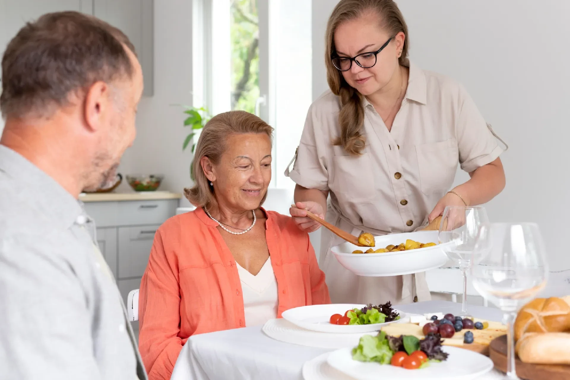 A woman serving a healthy meal to an elderly woman, with snacks and beverages available for residents in a care facility.