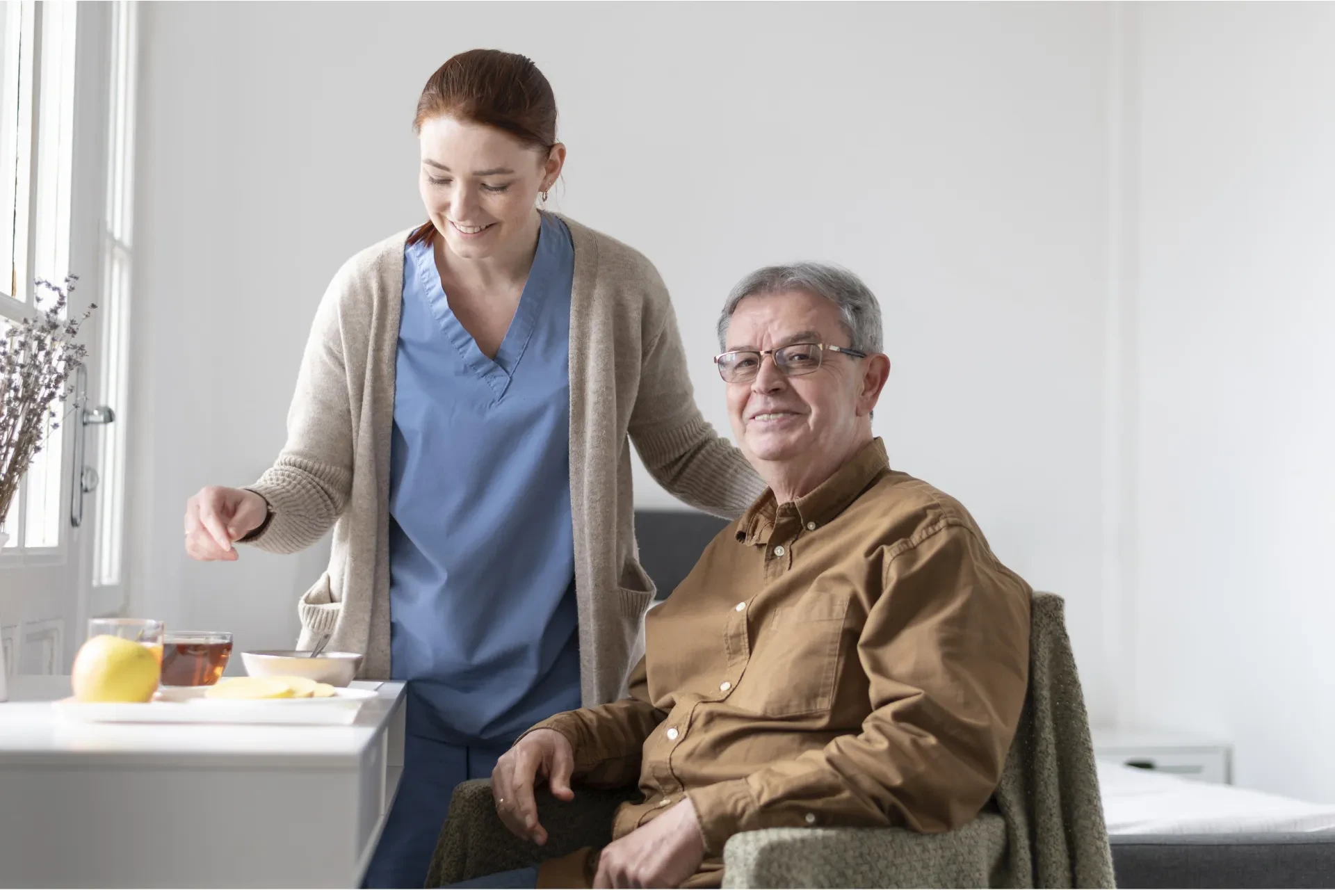 A caregiver and an elderly man enjoying a meal together in a social dining setting at an assisted living facility.